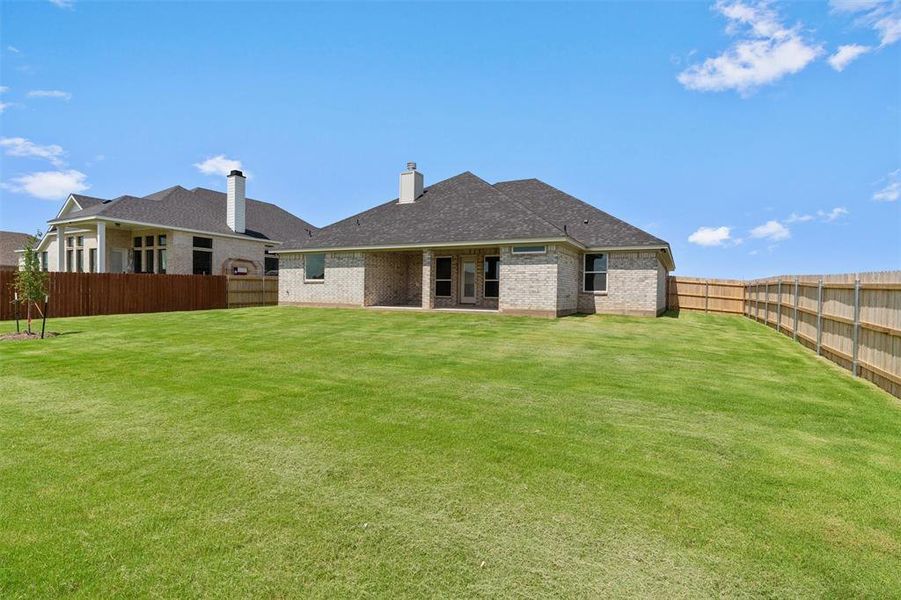 Expansive backyard featuring a large green lawn, full privacy fencing, and an attached covered patio Expansive backyard featuring a large green lawn, full privacy fencing, and an attached covered patio