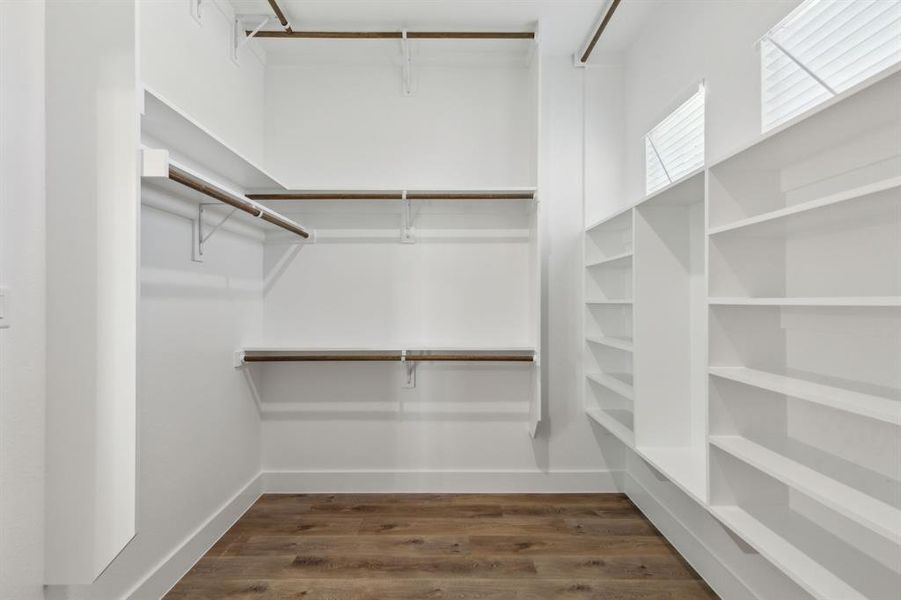 Spacious walk-in closet featuring wood-finish flooring, white walls, built-in shelving, hanging rods, and integrated windows with blinds