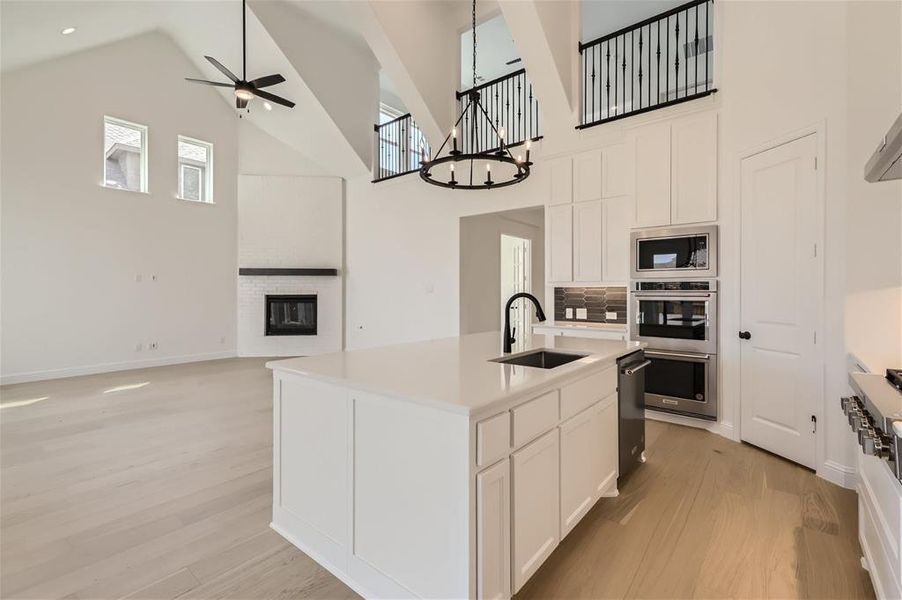 Kitchen featuring an island with sink, stainless steel appliances, light wood-type flooring, high vaulted ceiling, and sink