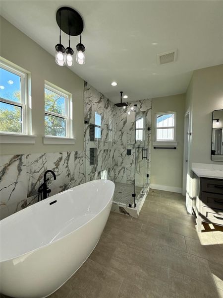 This bathroom features a modern design with a freestanding bathtub and a glass-enclosed shower. The space is accented by marble-patterned tiles and ample natural light from multiple windows. Contemporary lighting and sleek fixtures complete the elegant look. This bathroom features a modern design with a freestanding bathtub and a glass-enclosed shower. The space is accented by marble-patterned tiles and ample natural light from multiple windows. Contemporary lighting and sleek fixtures complete the elegant look.