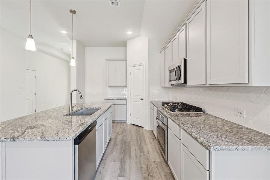 Kitchen with tasteful backsplash, light hardwood / wood-style floors, appliances with stainless steel finishes, pendant lighting, and sink