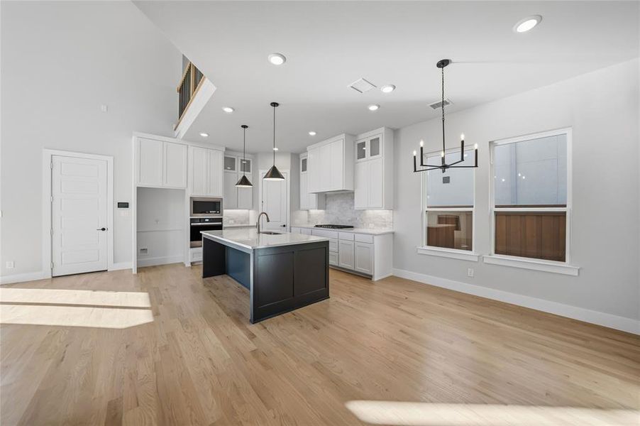 Kitchen with white cabinets, glass insert cabinets, a chandelier, decorative backsplash, and an island with sink