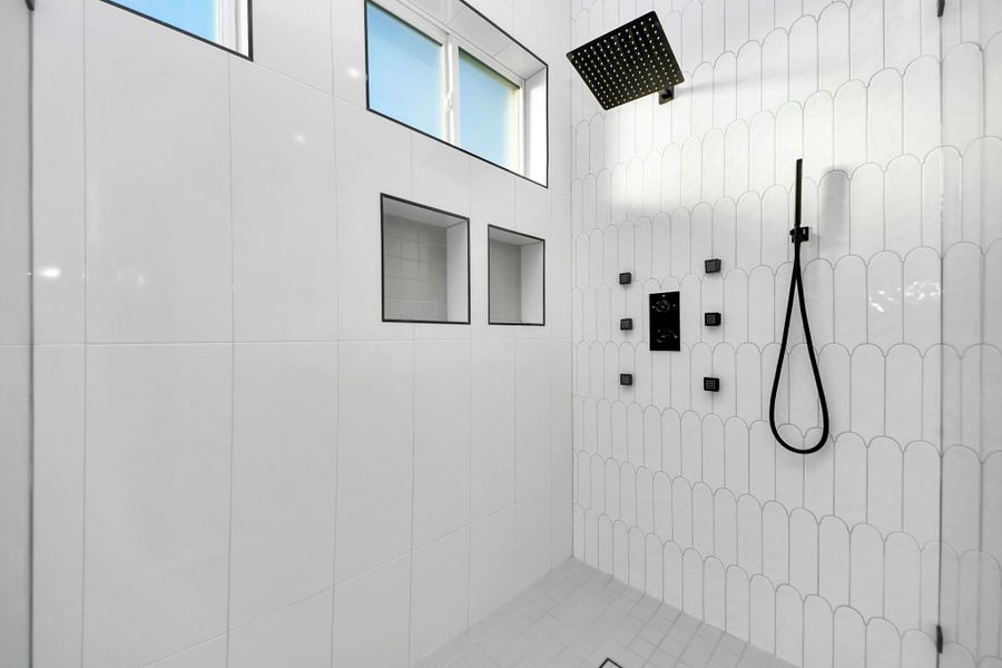 An accent wall within the shower features arched tiles, adding beautiful texture and detail. The luxurious shower set includes body sprayers, a rainfall showerhead, and a handheld shower, creating a spa-like experience. An accent wall within the shower features arched tiles, adding beautiful texture and detail. The luxurious shower set includes body sprayers, a rainfall showerhead, and a handheld shower, creating a spa-like experience.