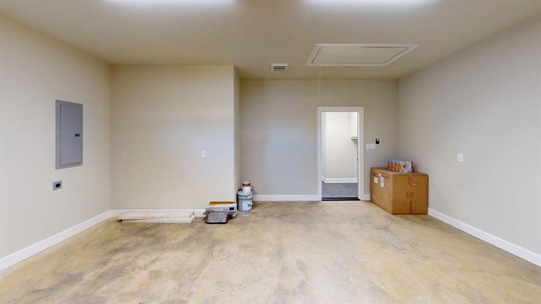 Spare room featuring electric panel, attic access, baseboards, and concrete floors