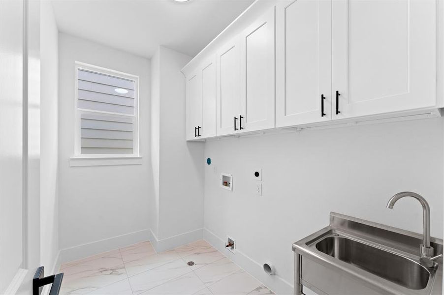 This photo showcases a bright, modern laundry room with white cabinetry, a stainless steel utility sink, and tiled flooring. The space is well-lit, featuring a window for natural light.