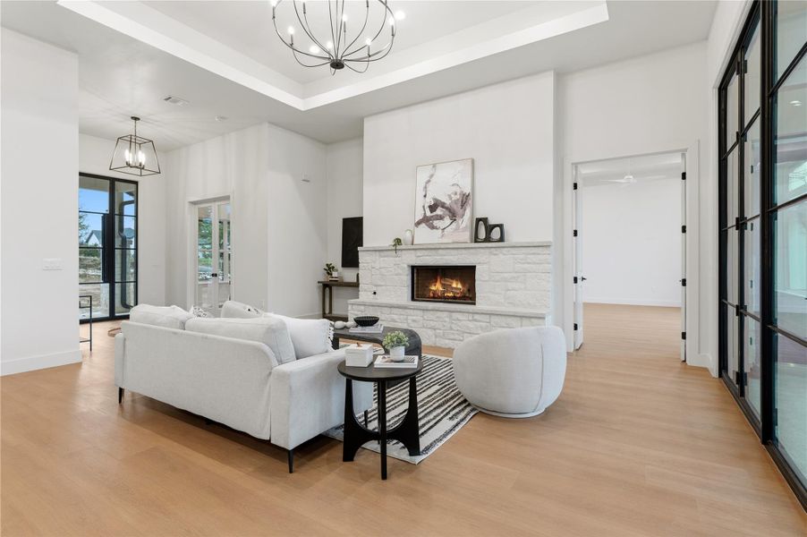 Living area featuring a chandelier, a stone fireplace, light wood-type flooring, and a high ceiling