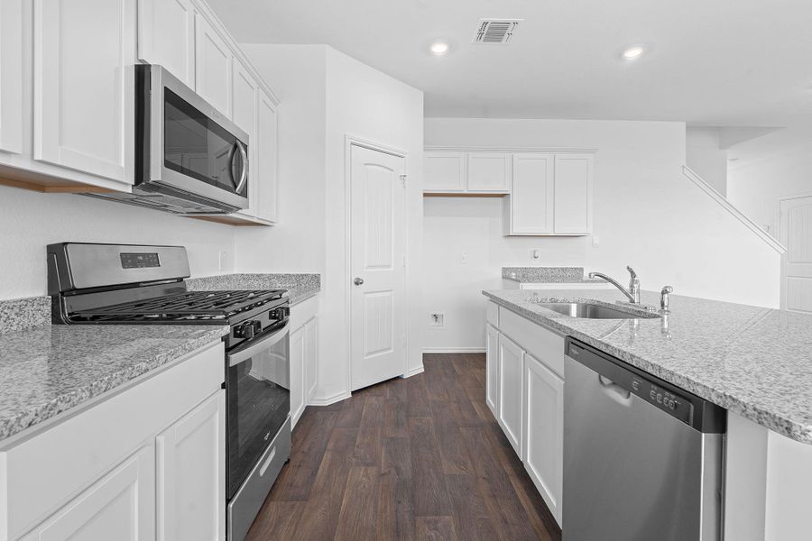 Kitchen featuring stainless steel appliances, dark wood-style flooring, white cabinets, recessed lighting, and light stone countertops Kitchen featuring stainless steel appliances, dark wood-style flooring, white cabinets, recessed lighting, and light stone countertops