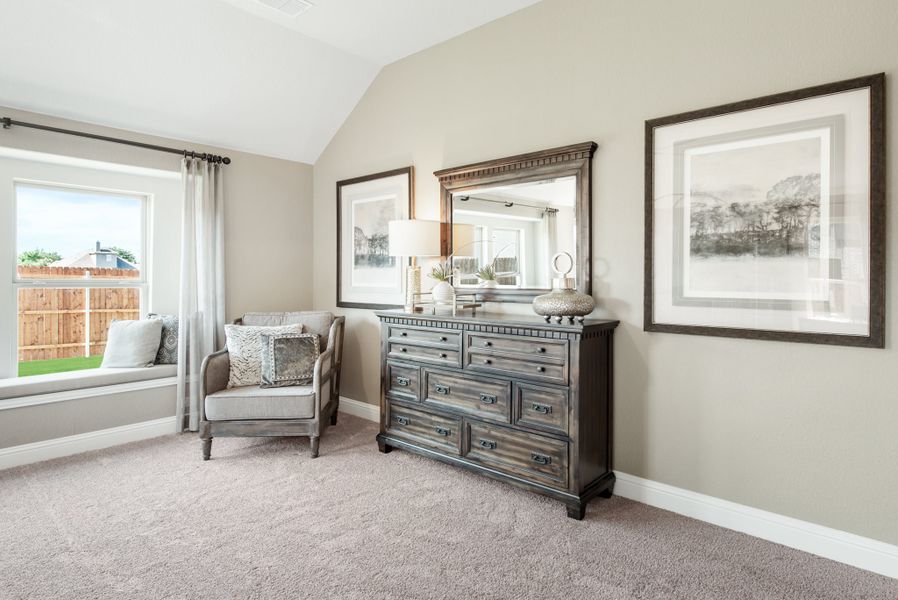 Bedroom with vaulted ceiling, dark wood dresser, accent chair, and window seat overlooking backyard
