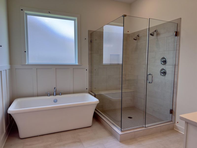 Freestanding soaking tub with chrome fixtures, glass-enclosed shower with tiled walls, shower bench, and two shower heads Freestanding soaking tub with chrome fixtures, glass-enclosed shower with tiled walls, shower bench, and two shower heads