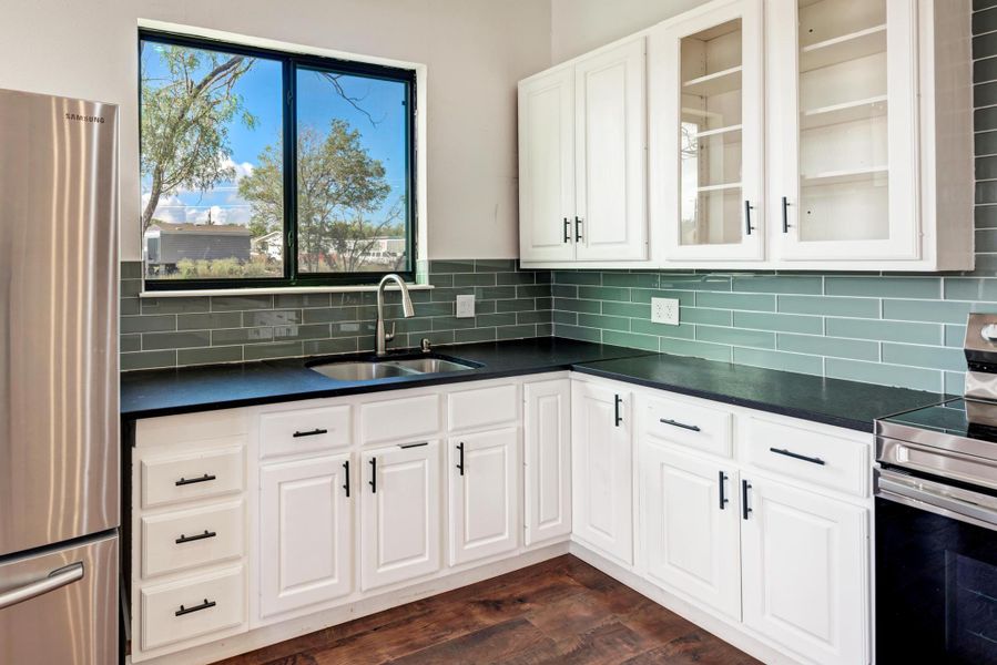 Dark countertops contrast with white cabinetry and a glass tile backsplash beneath the window.