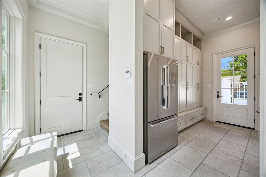 Spacious, well-appointed mudroom featuring tumbled limestone flooring and wall of custom built-in cabinetry for added storage and functionality. Includes a stainless refrigerator/freezer, a conveniently located half bath, and a staircase leading to the spacious mother-in-law or guest suite!