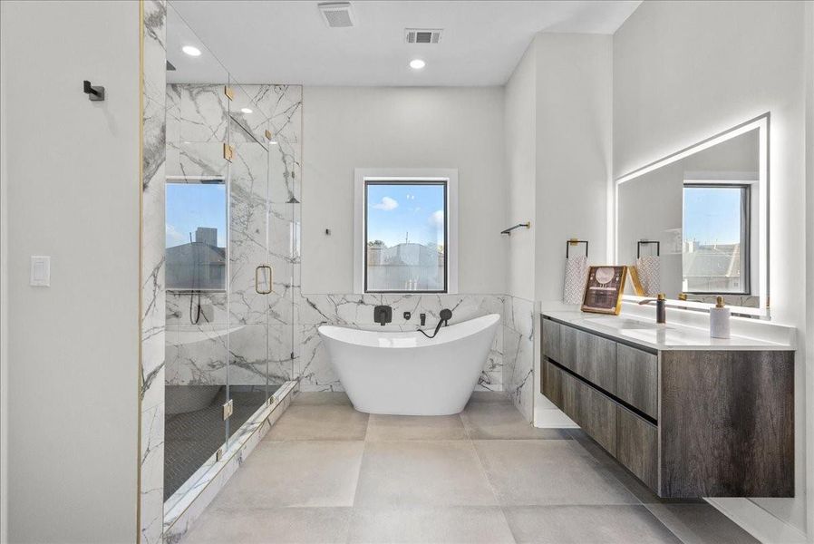 The primary bathroom feels like a private spa, featuring an oversized walk-in shower with multiple heads, a soothing rain feature, floor-to-ceiling porcelain tile, and a beautiful garden tub for relaxing at the end of the day.