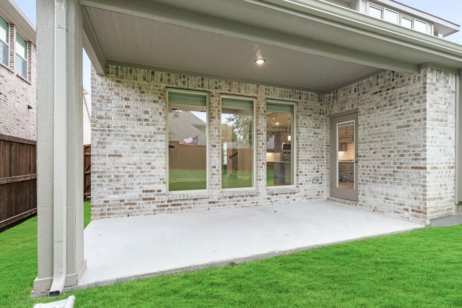 Covered back patio with concrete slab, brick exterior, large windows, and green lawn Covered back patio with concrete slab, brick exterior, large windows, and green lawn
