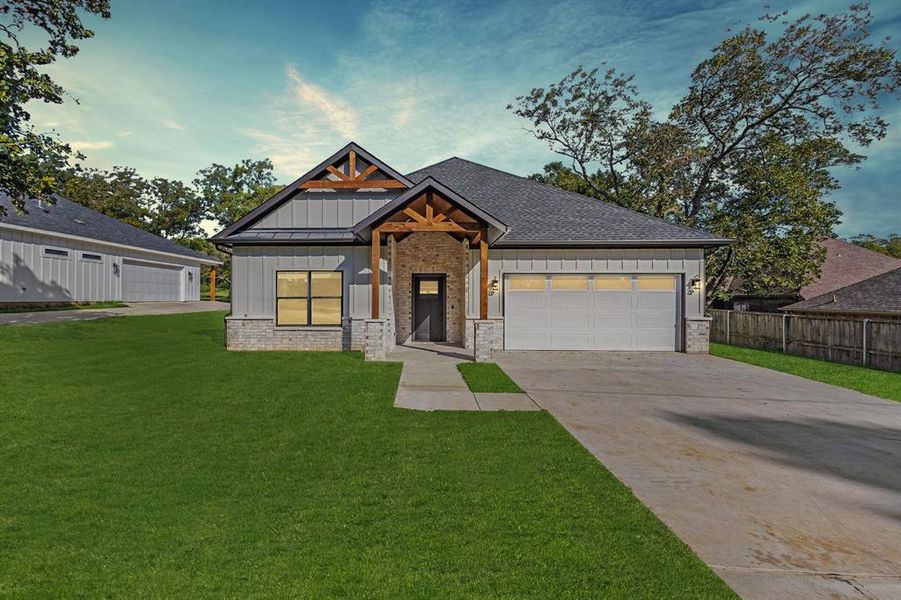 View of front of house featuring board and batten siding, brick siding, concrete driveway, and roof with shingles