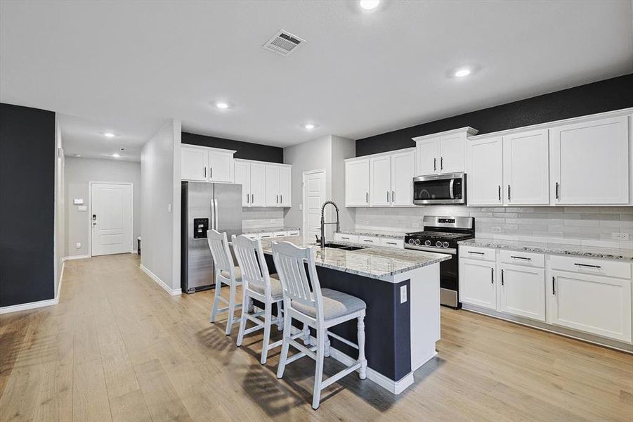 Kitchen with sink, white cabinetry, stainless steel appliances, light stone counters, and an island with sink