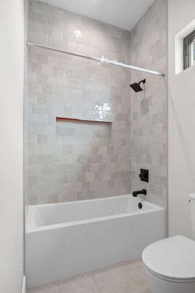 Bathtub with light gray subway tile surround featuring a recessed niche, matte black shower head, and matching faucet