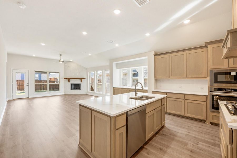 Open kitchen with center island, light wood cabinets, and stainless appliances, open to living room with fireplace and hardwood floors Open kitchen with center island, light wood cabinets, and stainless appliances, open to living room with fireplace and hardwood floors