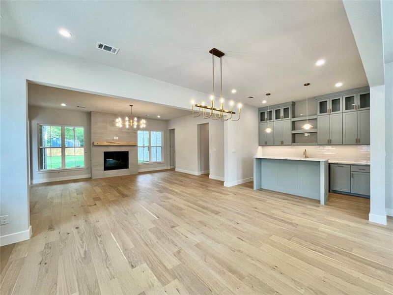 Kitchen featuring decorative light fixtures, gray cabinets, a large fireplace, an inviting chandelier, and light hardwood / wood-style floors