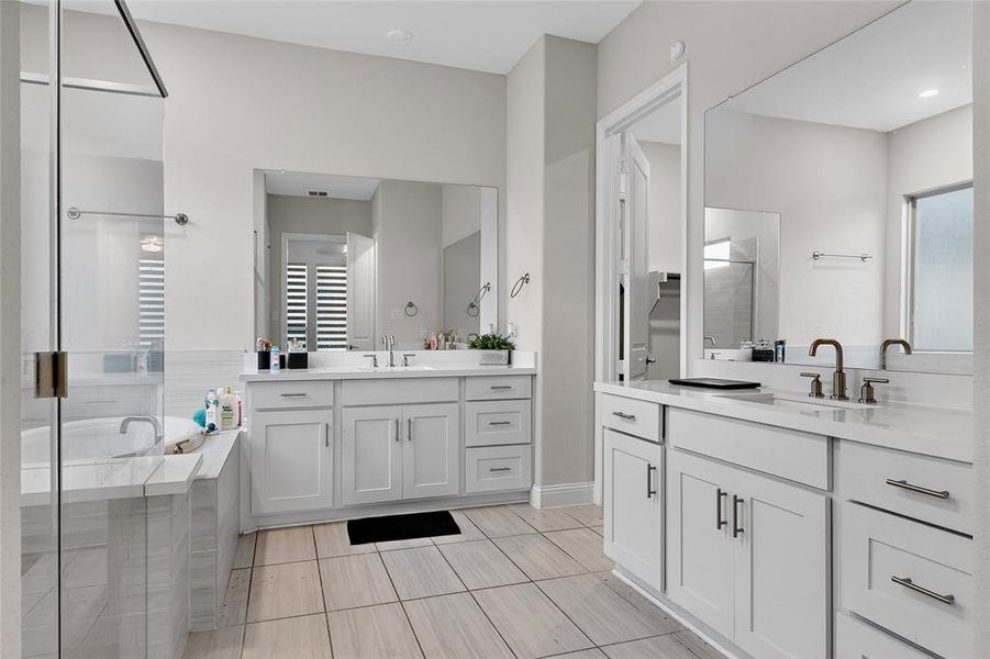 Full bath featuring a bath, two vanities, a stall shower, and light tile patterned flooring