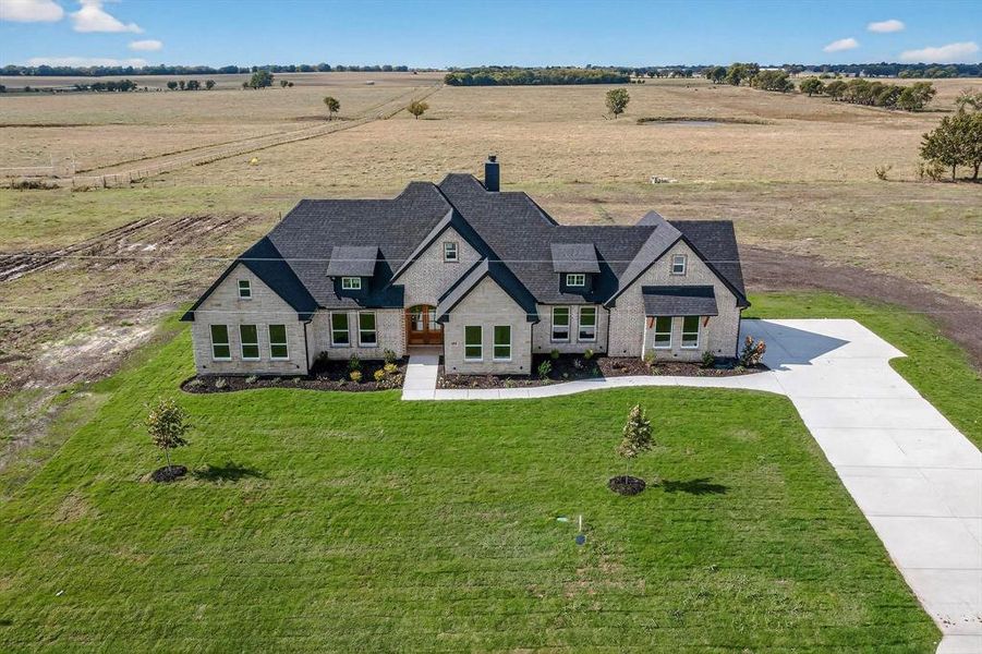 View of front of home featuring a front yard, concrete driveway, stone siding, a chimney, and a view of rural / pastoral area View of front of home featuring a front yard, concrete driveway, stone siding, a chimney, and a view of rural / pastoral area