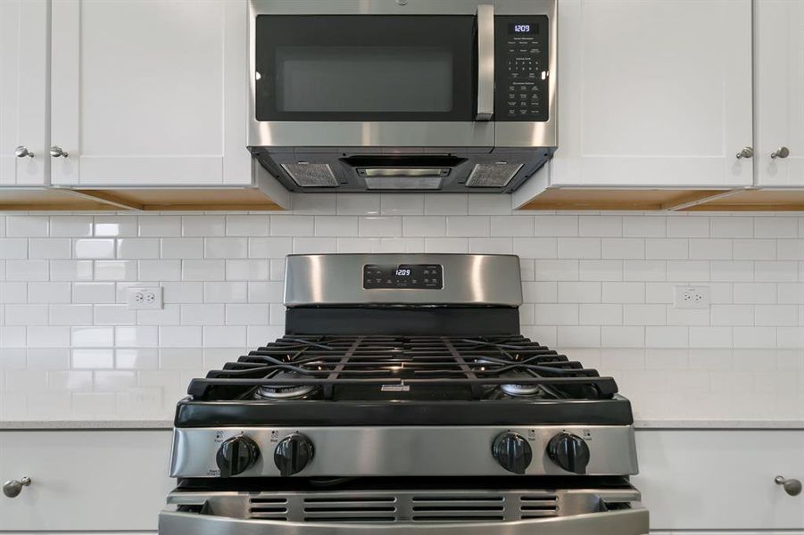 Kitchen featuring backsplash, appliances with stainless steel finishes, white cabinetry, and light stone counters