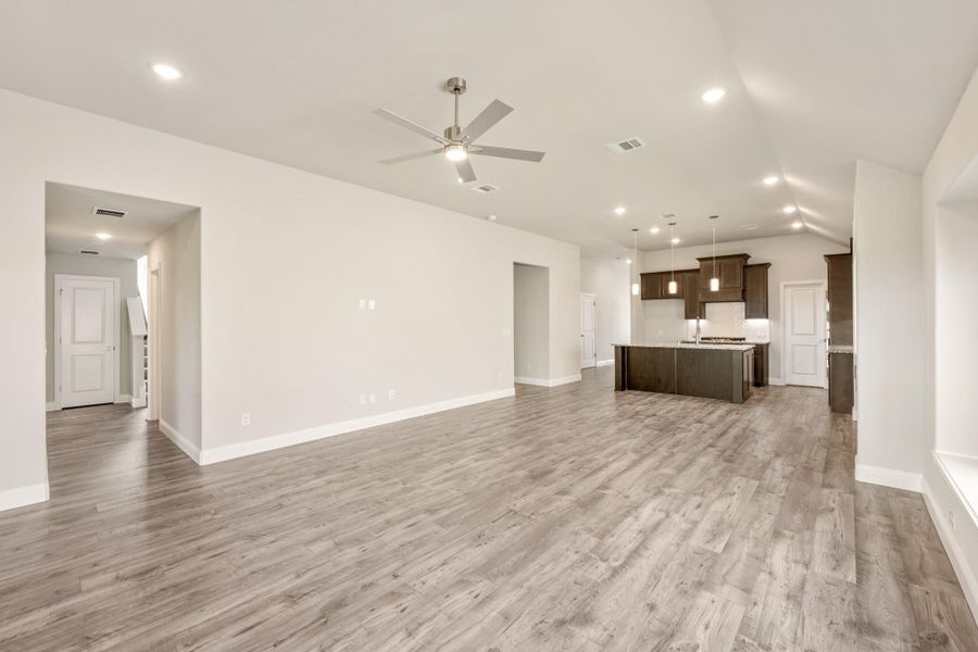 Open living area with wood-look floors and ceiling fan, open to kitchen with dark cabinets and island