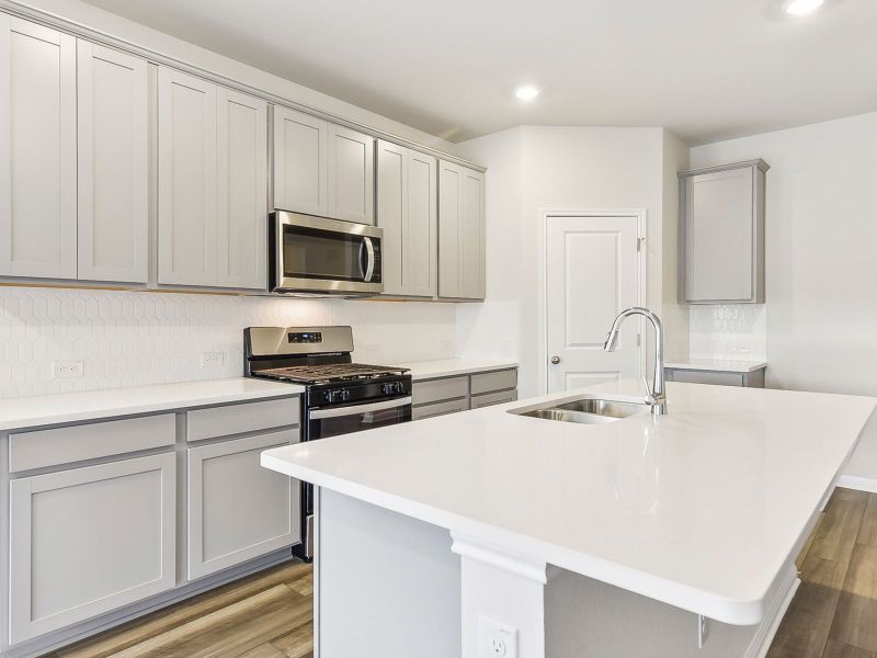 The kitchen features stone colored cabinets and quartz countertops.