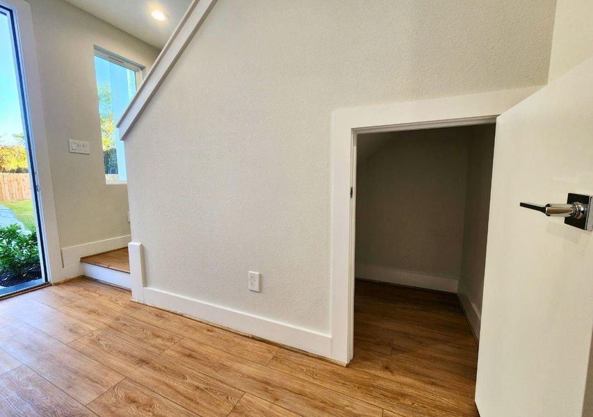 This photo shows a bright entryway with wood flooring. There's a small, open door under the staircase, ideal for storage. Natural light flows in from a nearby window and glass door, leading to a garden outside. This photo shows a bright entryway with wood flooring. There's a small, open door under the staircase, ideal for storage. Natural light flows in from a nearby window and glass door, leading to a garden outside.