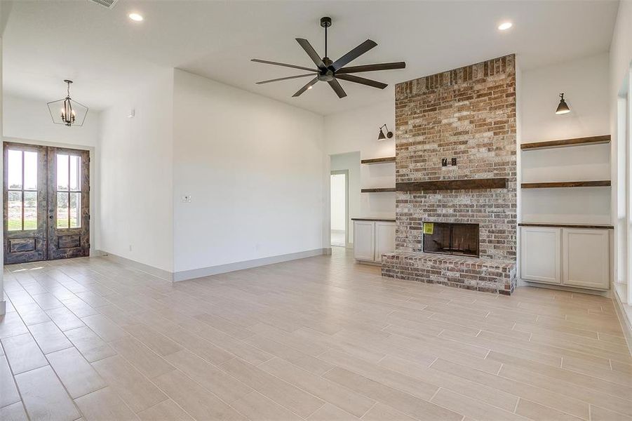 Unfurnished living room featuring light hardwood / wood-style floors, french doors, ceiling fan with notable chandelier, and a fireplace