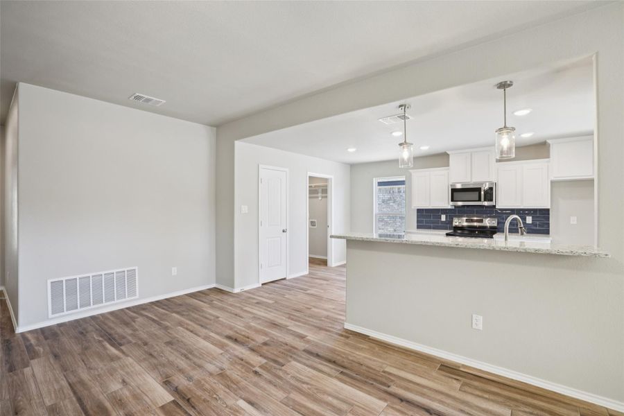 Kitchen with white cabinets, pendant lighting, stainless steel appliances, light wood-type flooring, and light stone counters