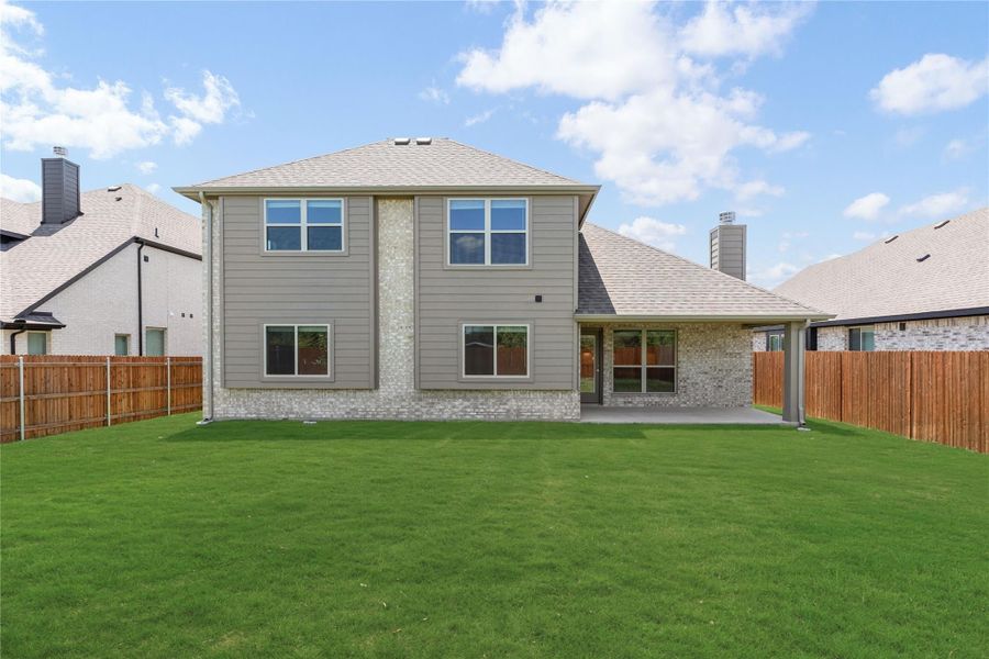Two-story home rear view with covered patio, brick and siding exterior, and fenced backyard with green lawn