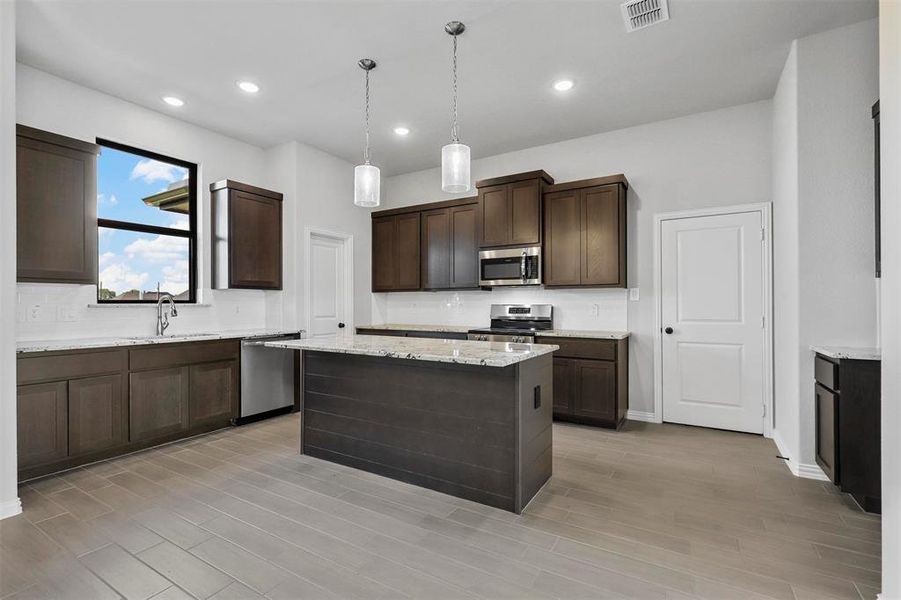 Kitchen featuring dark brown cabinets, pendant lighting, a kitchen island, and stainless steel appliances