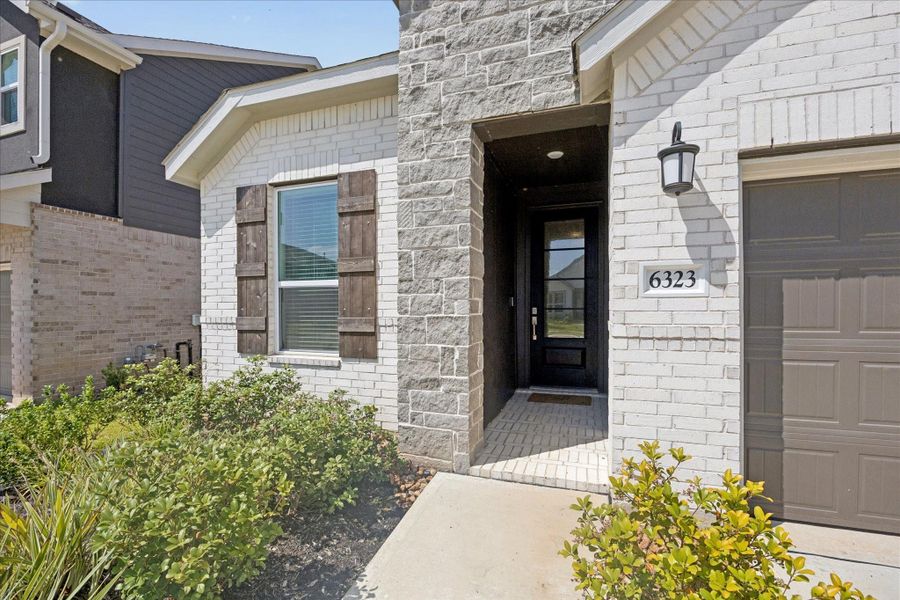 Curb appeal starts strong with a covered entry, handsome exterior lighting and a mix of brick, stone and warm accents that set the tone for the stylish spaces waiting inside.