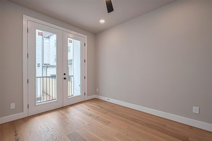 Bright and airy room with light wood floors, neutral walls, and large glass doors opening to a cozy balcony. Enhanced by recessed lighting for a modern touch.