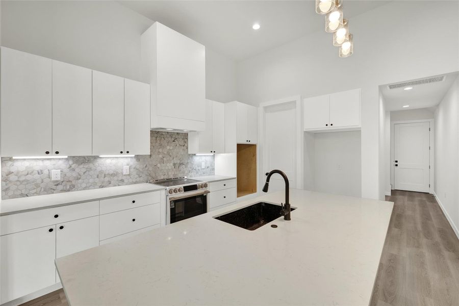Kitchen featuring range with electric cooktop, light stone countertops, white cabinetry, decorative backsplash, and an island with sink