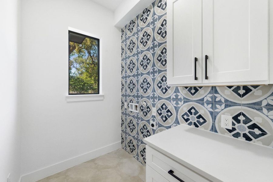 Downstairs laundry room with light tile patterned floors and cabinetry