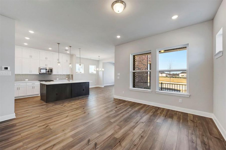 Kitchen featuring open floor plan, an island with sink, stainless steel microwave, backsplash, and suspended lighting