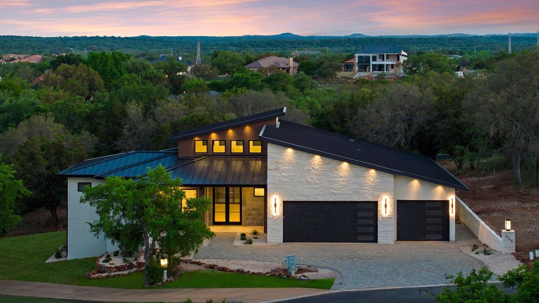 Modern architecture shines with a striking facade, well-lit entrance, and a paver driveway.
