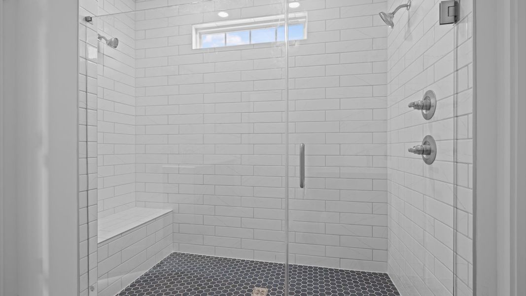 Notable primary bath featuring two vanities, tiled walk-in shower, and tasteful design touches throughout