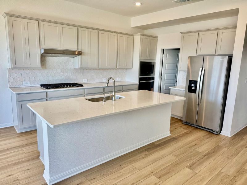 Kitchen with tasteful backsplash, stainless steel appliances, light stone countertops, light wood-style floors, and a center island with sink Kitchen with tasteful backsplash, stainless steel appliances, light stone countertops, light wood-style floors, and a center island with sink