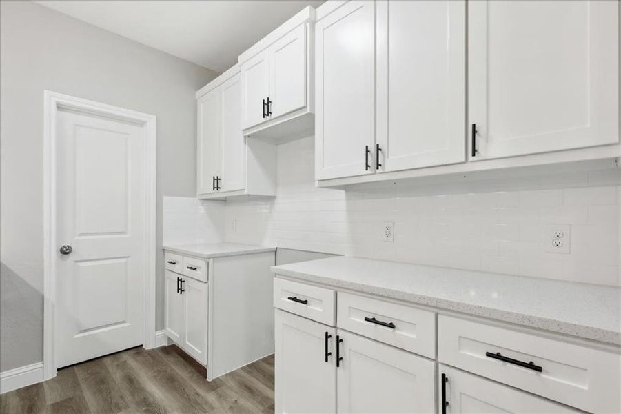 Kitchen featuring white cabinetry, tasteful backsplash, hardwood / wood-style flooring, and light stone countertops