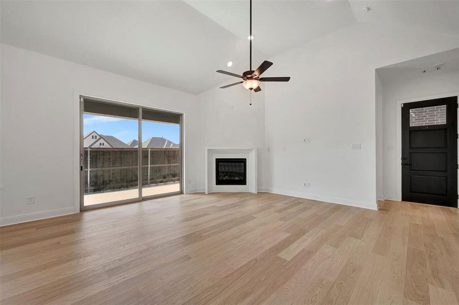 Unfurnished living room featuring a ceiling fan, a glass covered fireplace, light wood-style flooring, and vaulted ceiling Unfurnished living room featuring a ceiling fan, a glass covered fireplace, light wood-style flooring, and vaulted ceiling
