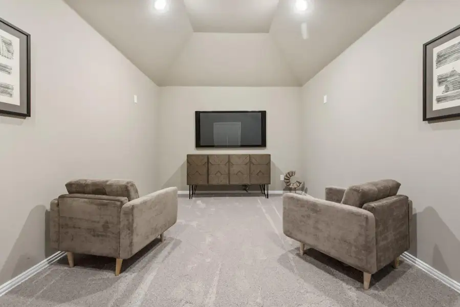 Media room with vaulted ceiling, two armchairs, wall-mounted TV, and wood console cabinet on carpet flooring