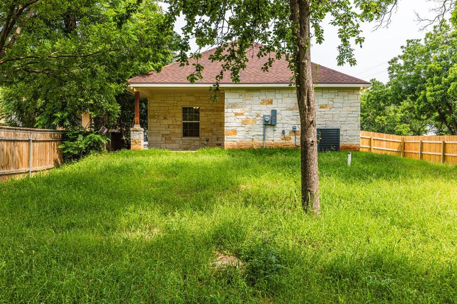 Rear view of property featuring stone siding, a fenced backyard, and a shingled roof