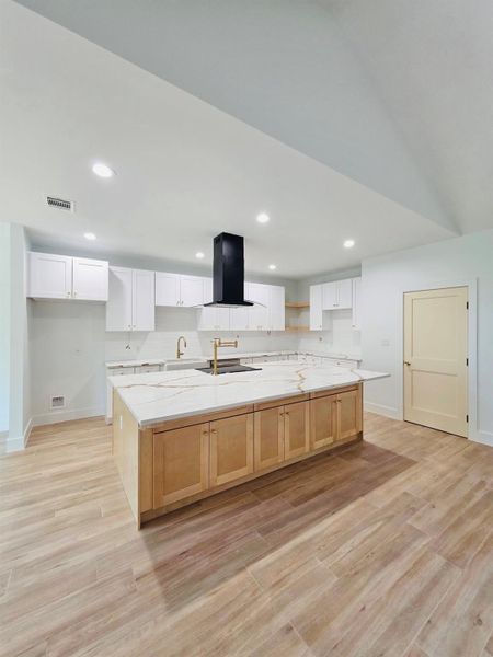 Kitchen with white cabinets, a large island with sink, light wood finished floors, recessed lighting, and light stone countertops