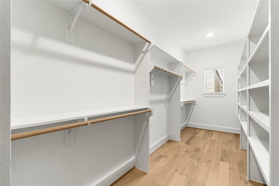 Spacious walk-in closet with ample shelving and hanging space, featuring a window for natural light and wood flooring.