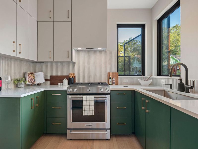 Kitchen with green cabinetry, stainless steel range with gas stovetop, white cabinetry, light wood-style flooring, and decorative backsplash