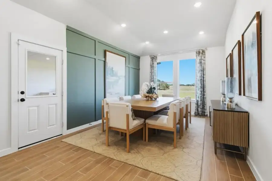 Dining room with wood table, eight chairs, green accent wall, and large window with outdoor view