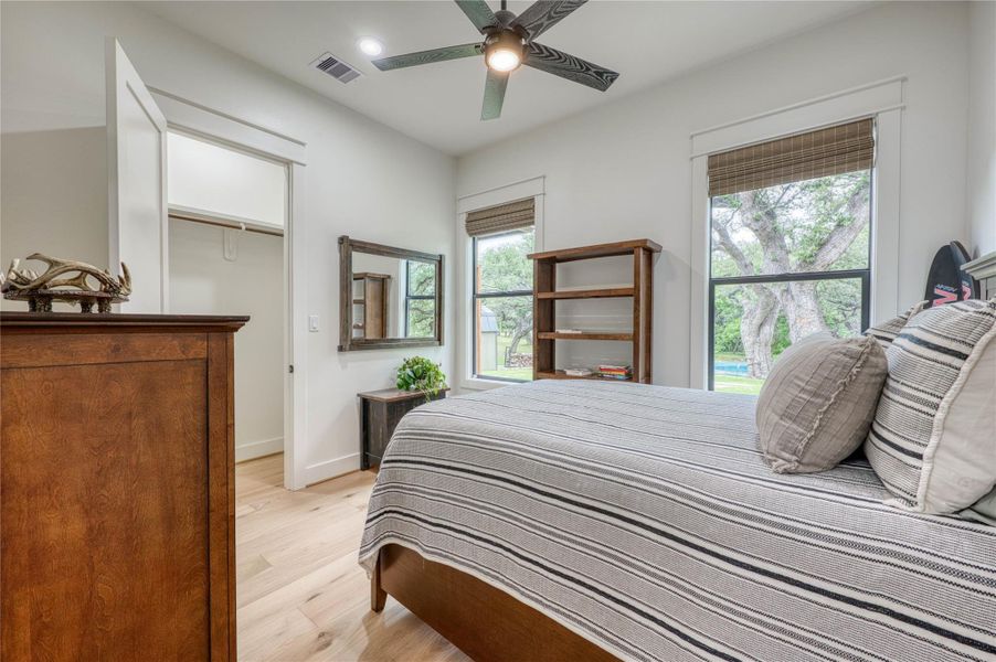 Bedroom featuring light wood-finish flooring, white walls, and a ceiling fan with integrated lighting