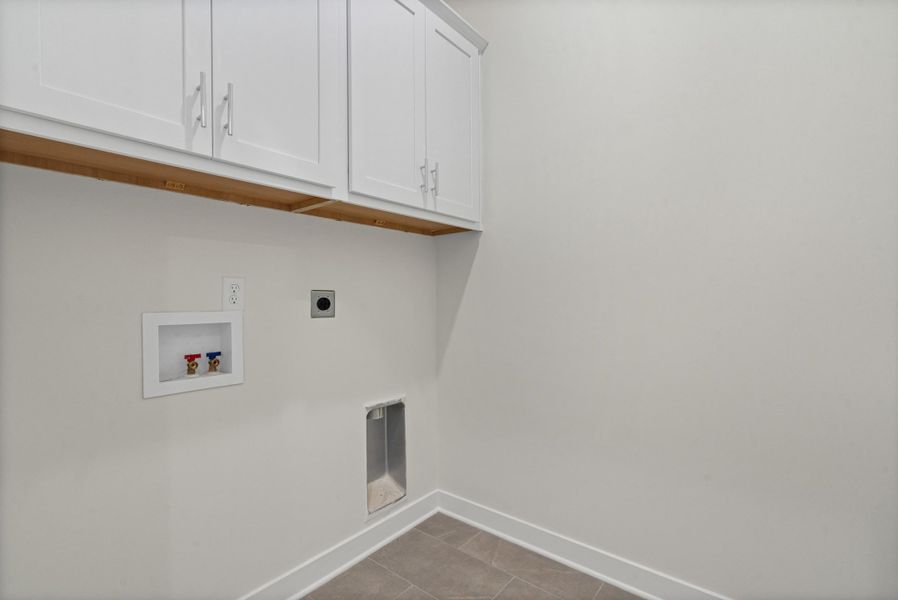 Laundry area with hookup for an electric dryer, washer hookup, cabinet space, and dark tile patterned flooring